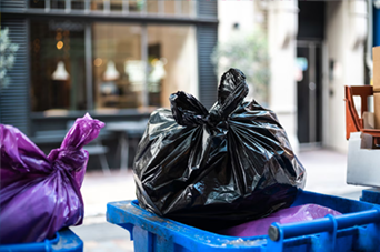 Man sawing wood in a workshop, wearing an apron, with wood scraps and tools.