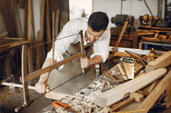 Woodworker using a bow saw to cut a wooden plank in a workshop.