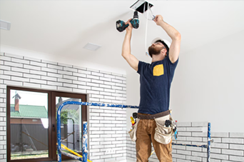Hands testing wires with a multimeter on a white terminal block on a wooden surface.