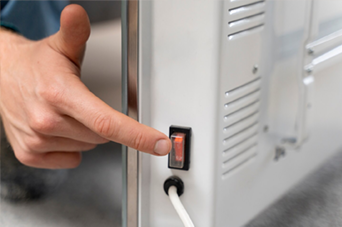 Person in orange safety vest and yellow hard hat using a paint roller on a white wall.