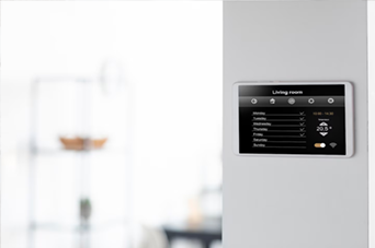 Person in orange safety vest and yellow hard hat using a paint roller on a white wall.