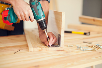 Man using a bow saw to cut wood in a workshop with tools and wood shavings.