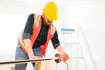 Person installing flooring, holding a plank covered with adhesive. Tools and bucket nearby.