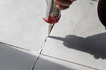 Person in orange safety vest and yellow hard hat using a paint roller on a white wall.