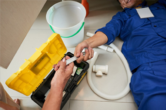 Person installing flooring, holding a plank covered with adhesive. Tools and bucket nearby.