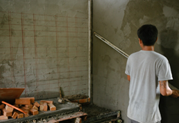 Man using a bow saw to cut wood in a workshop with tools and wood shavings.