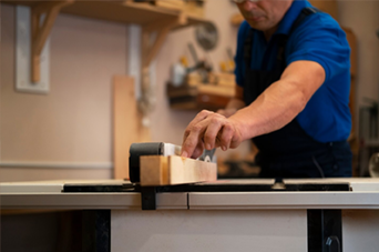 Man using a bow saw to cut wood in a workshop with tools and wood shavings.