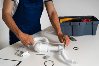 Person in orange safety vest and yellow hard hat using a paint roller on a white wall.