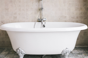 White clawfoot bathtub with shower fixtures against a tiled wall.