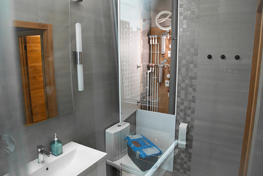 Modern bathroom with gray tiles, shower, toilet, and sink. Wooden door and mirror.