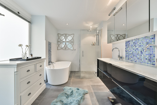 Modern bathroom with white and blue accents, featuring a soaking tub, vanity, and large window.