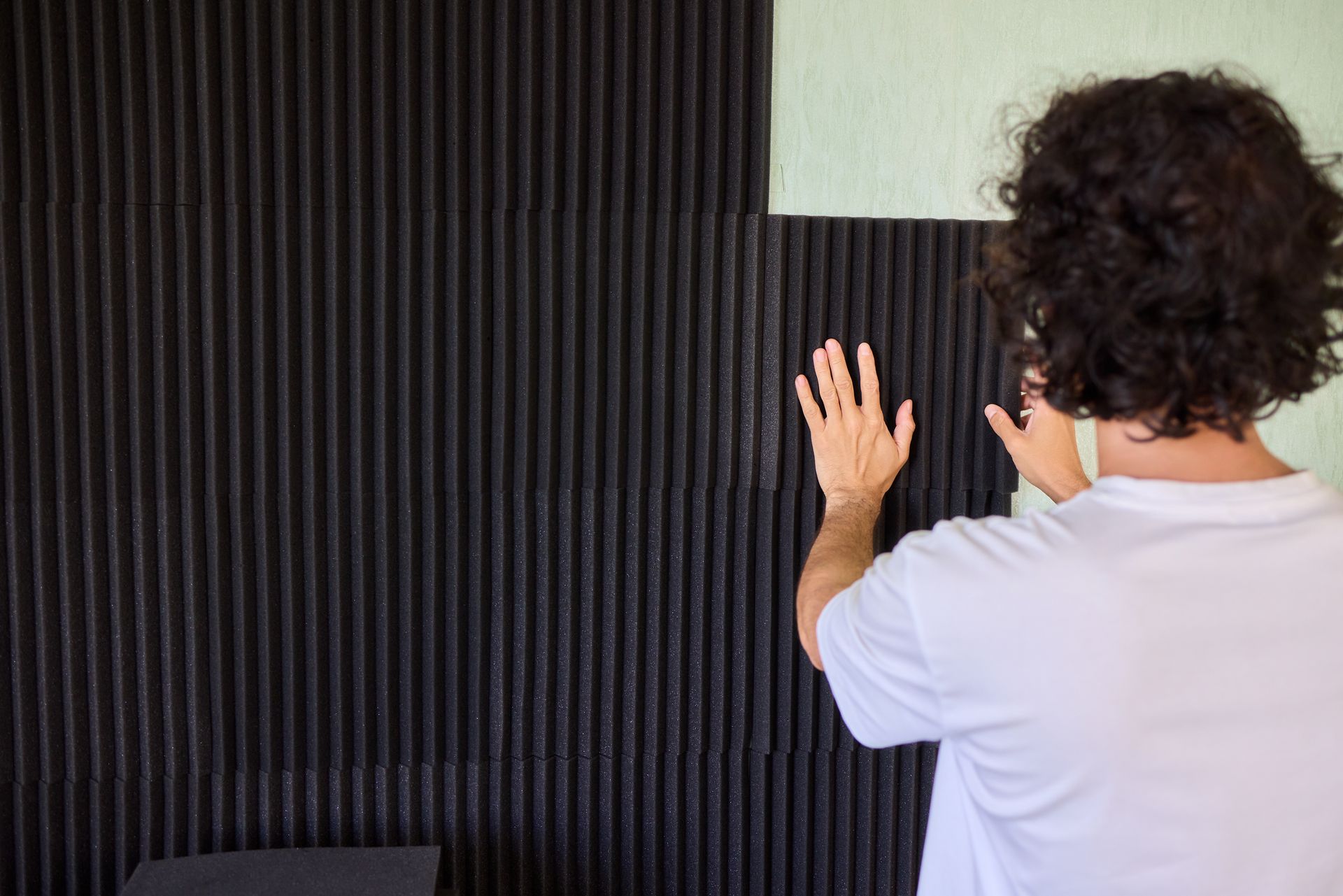 Person in orange safety vest and yellow hard hat using a paint roller on a white wall.