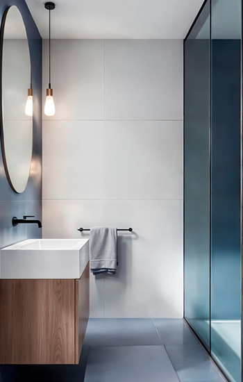Modern bathroom with blue and white walls, wood vanity, oval mirror, and glass shower.