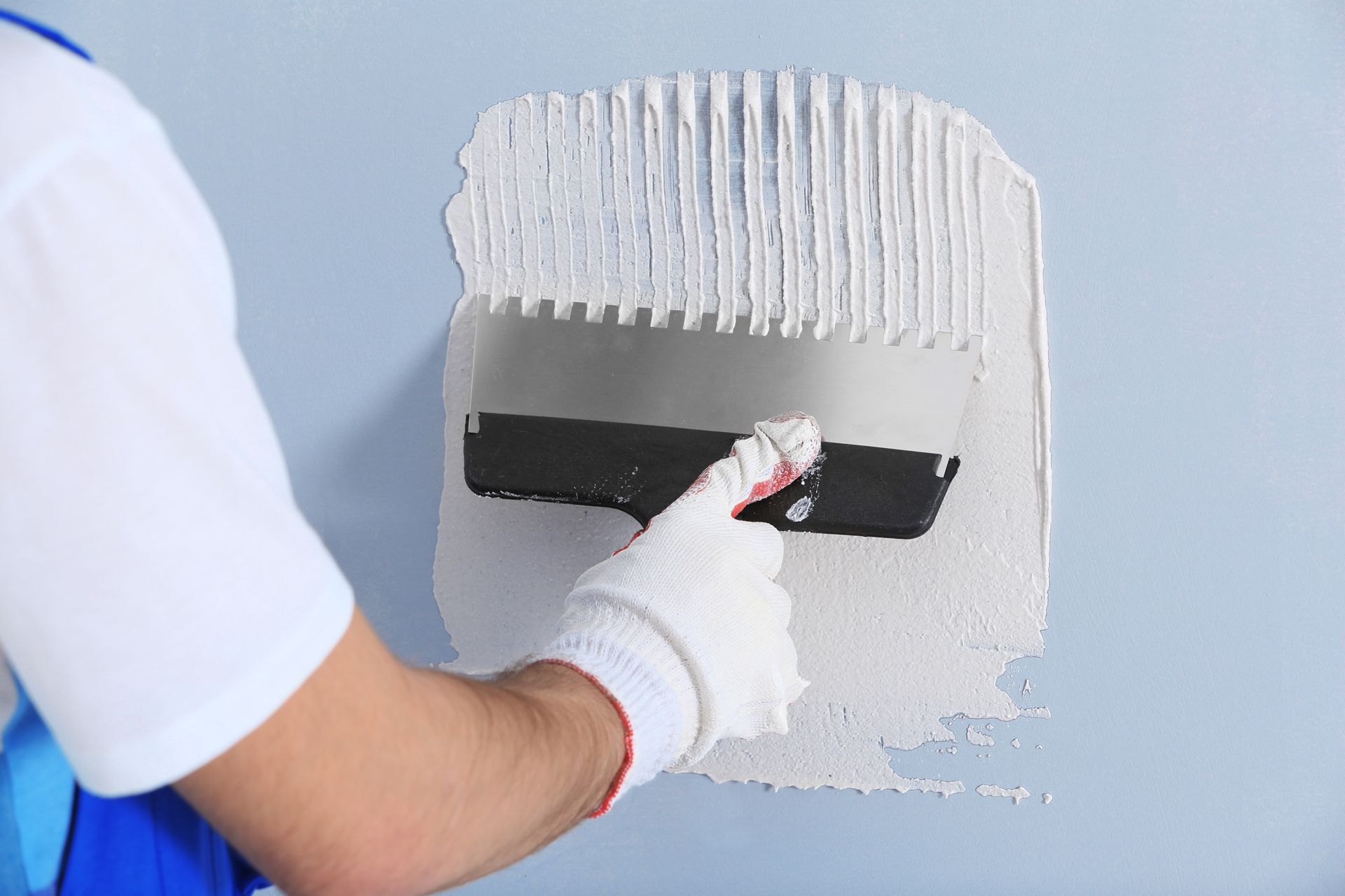 Person installing flooring, holding a plank covered with adhesive. Tools and bucket nearby.
