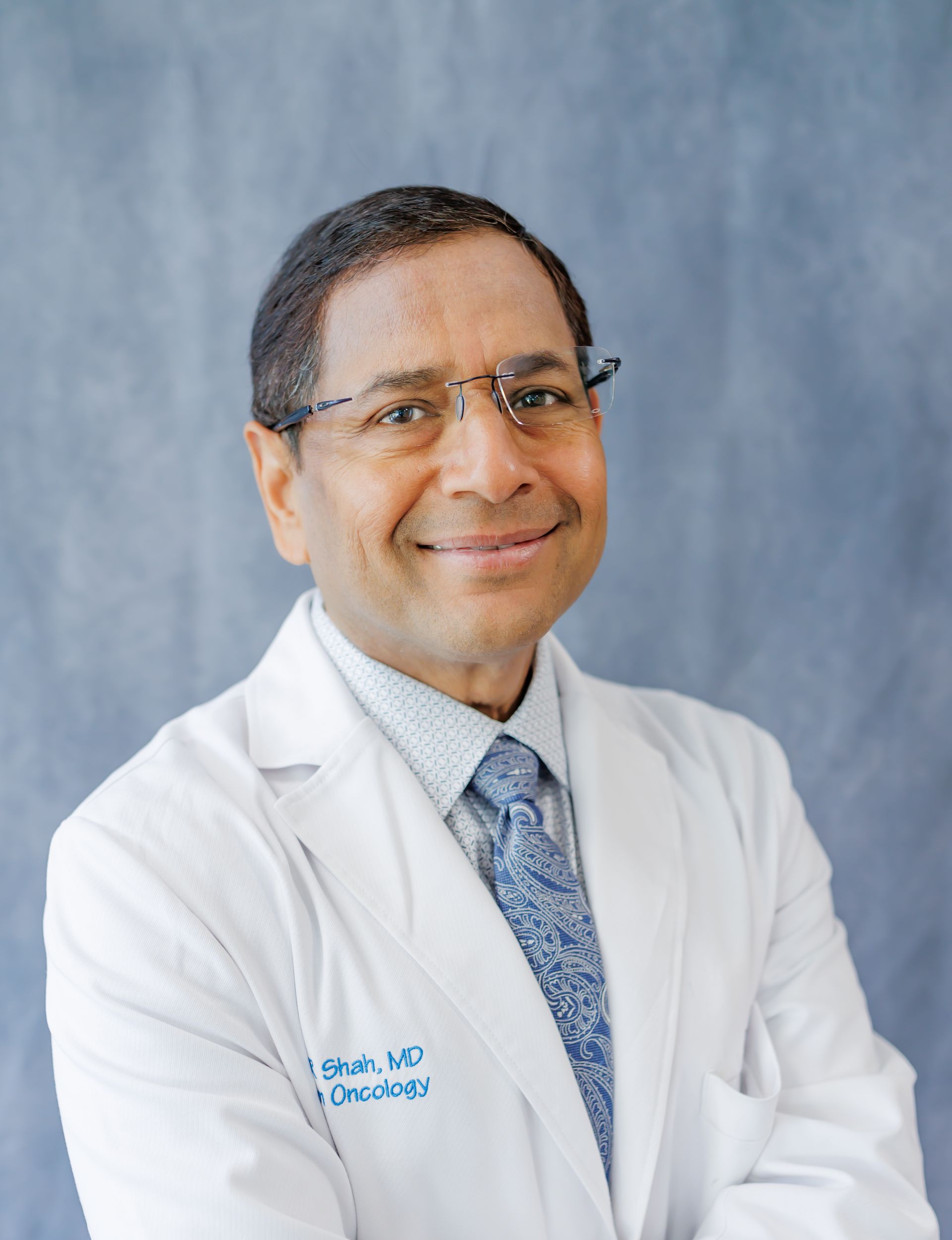 A man in a white coat and tie is smiling for the camera.