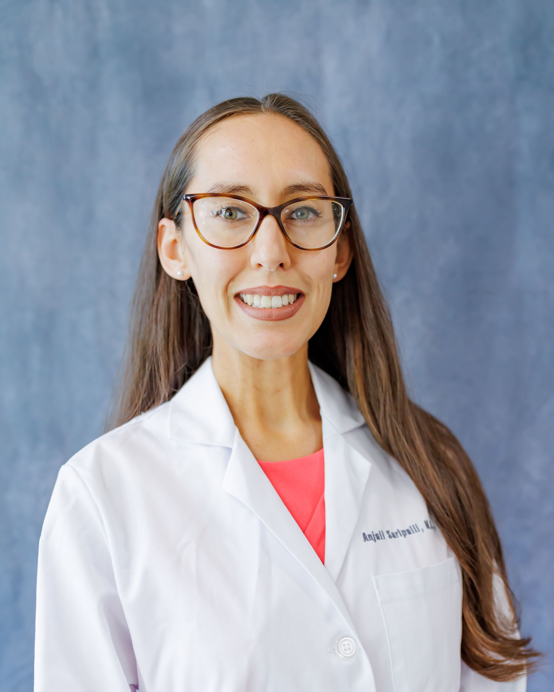 A woman wearing glasses and a white lab coat is smiling for the camera.