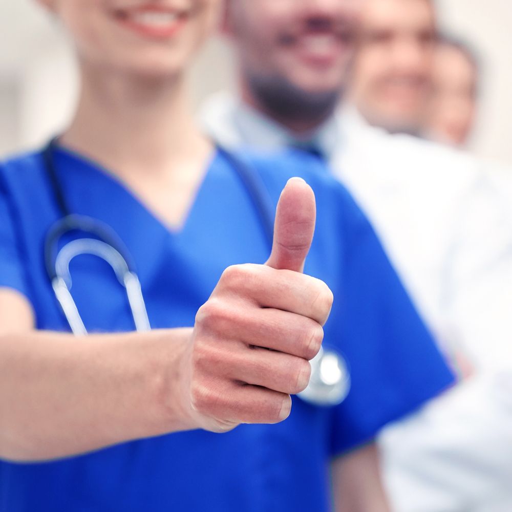 A nurse in a blue scrub is giving a thumbs up