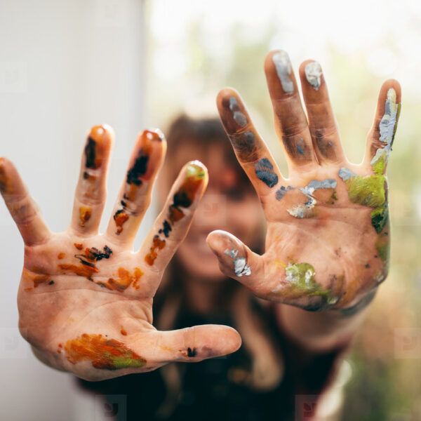 A person 's hands are covered in paint and are reaching out towards the camera.