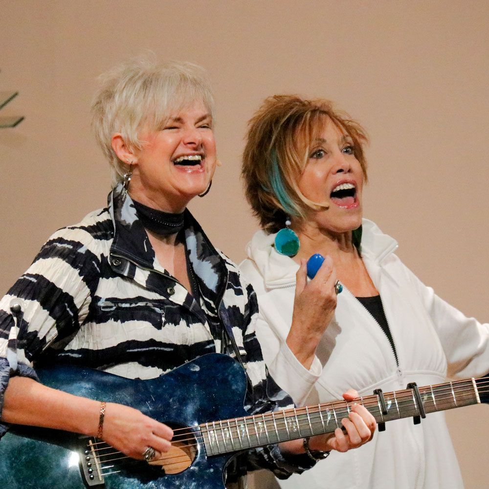 Two women are singing and playing guitars together