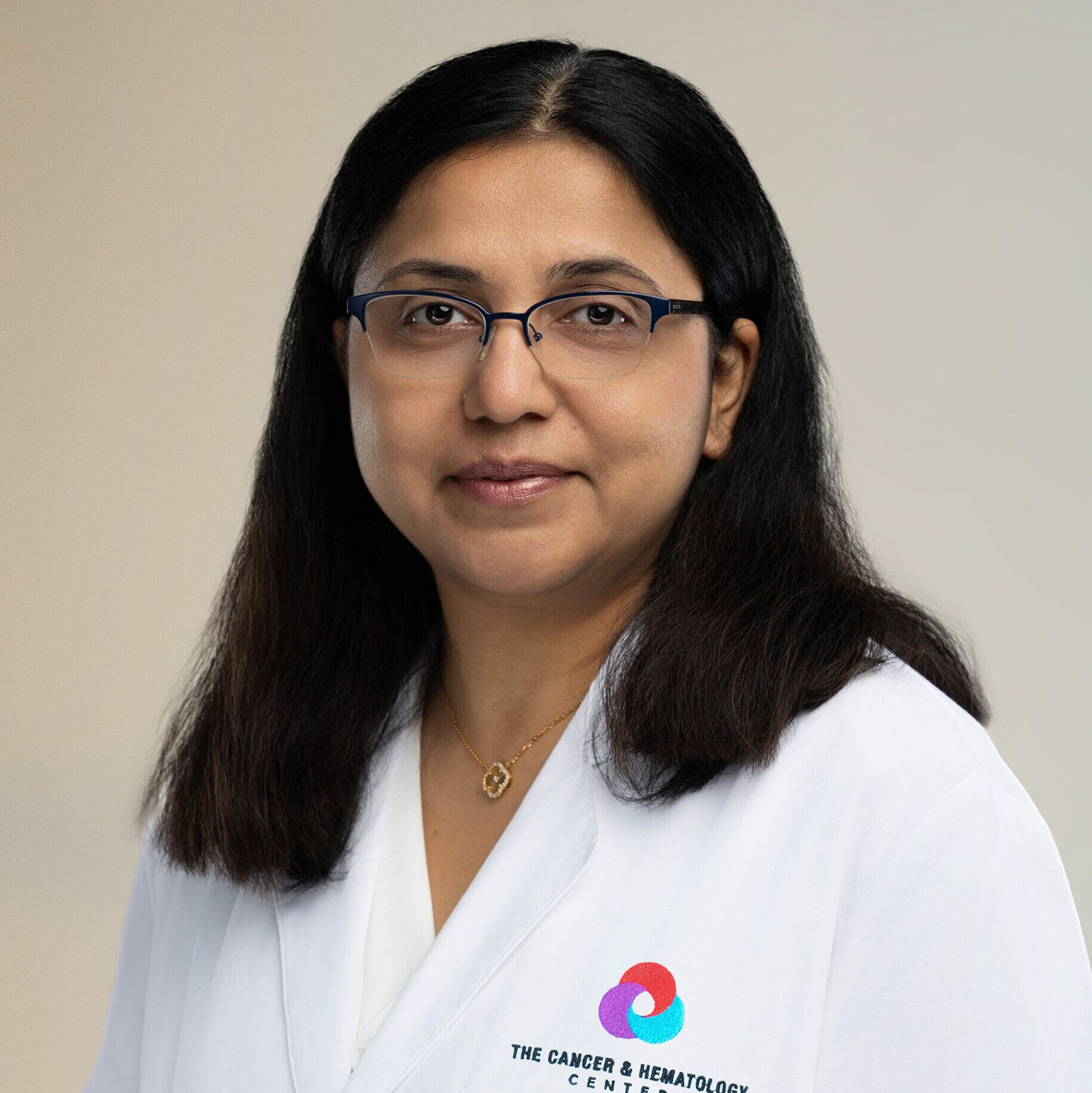 A woman wearing glasses and a white lab coat is looking at the camera.