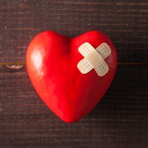 A red heart with a bandage on it is on a wooden table.