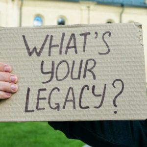 A person is holding a cardboard sign that says what 's your legacy