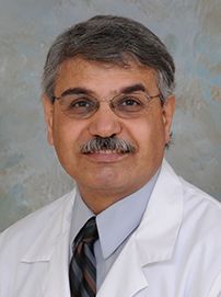 A man with a mustache and glasses is wearing a white coat and tie.