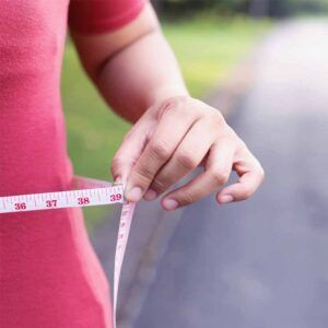 A woman is measuring her waist with a tape measure.