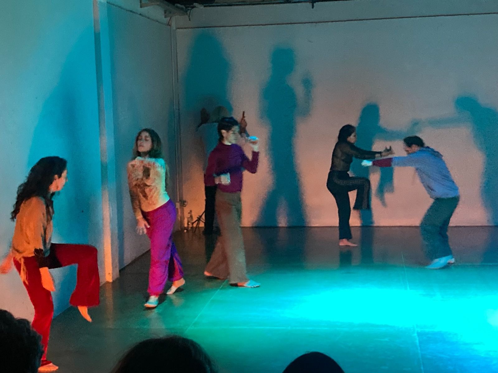 Cuatro bailarines interpretan una pieza contemporánea en un escenario con una iluminación azul vibrante y sombras dramáticas sobre una pared blanca.