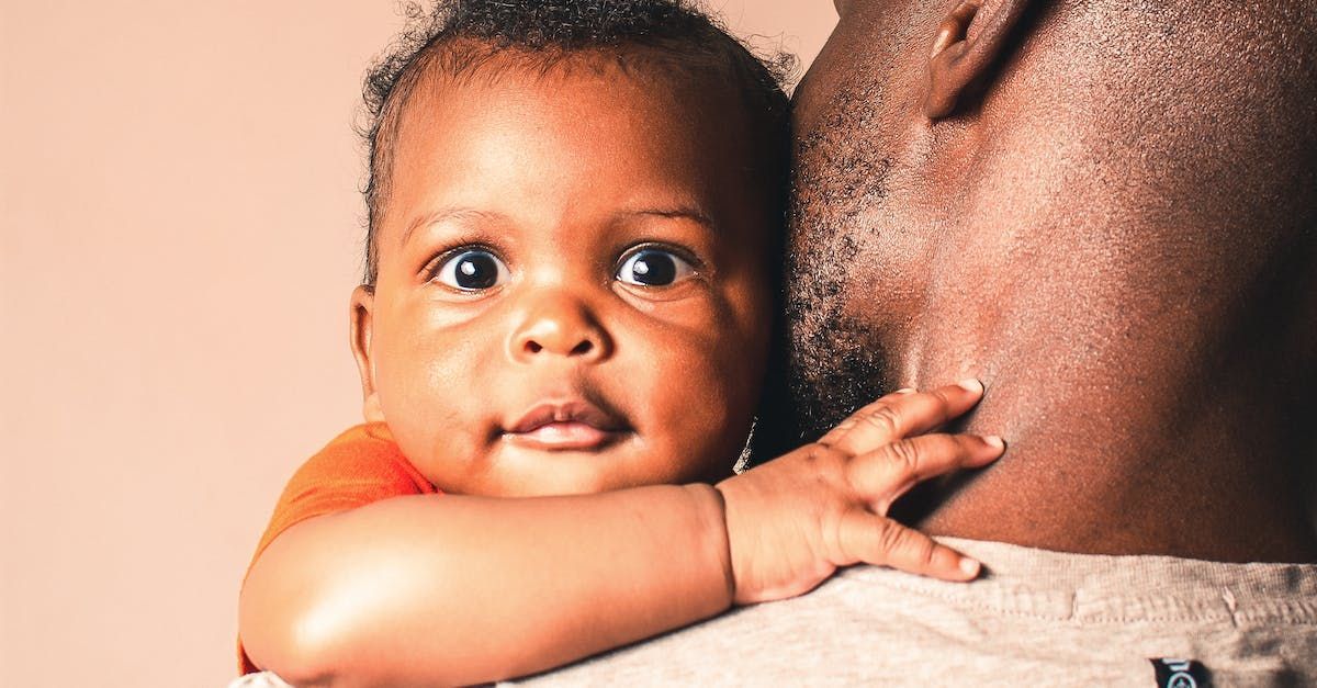 A photo of a black father holding his newborn bright eyed smiling baby.