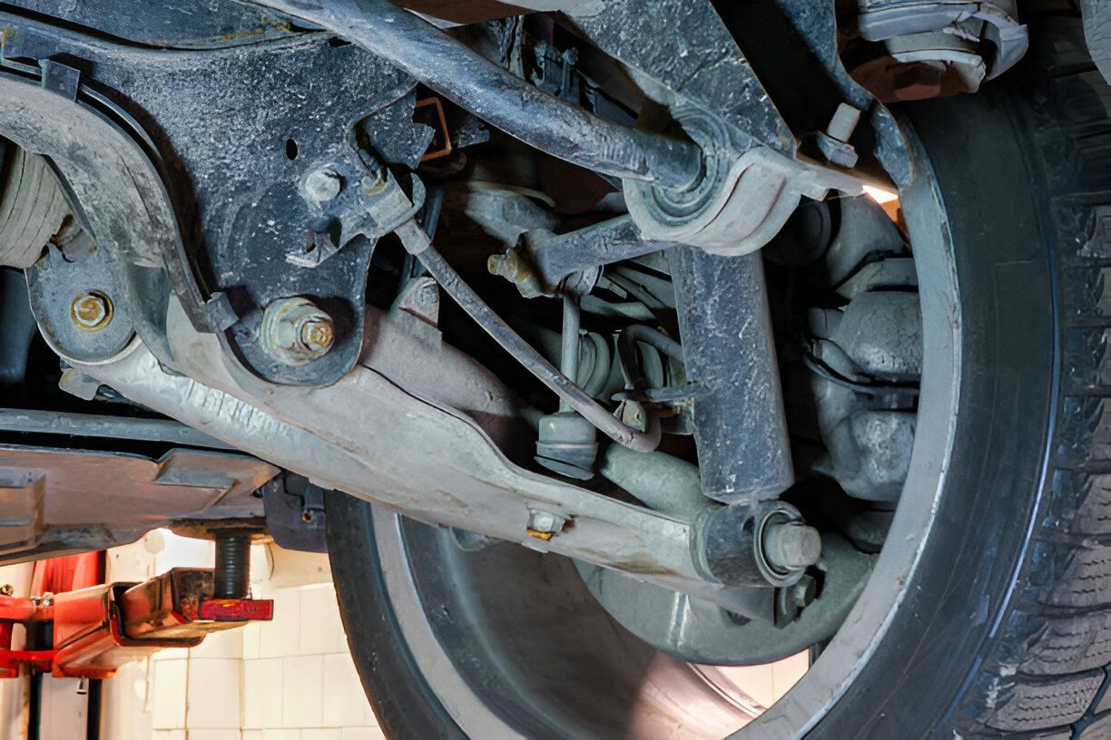 Car's rear suspension components, including shock absorber, control arms, and tire, viewed from below.