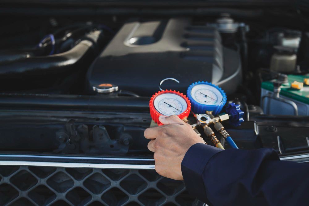 Person connecting gauges to a car's AC system in a garage.