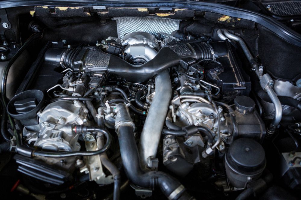 Close-up of a car engine with various black and silver components, including pipes, filters, and other mechanical parts.