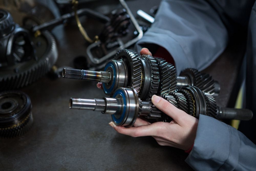 Hands holding car transmission gears. Mechanic's workspace, parts visible.