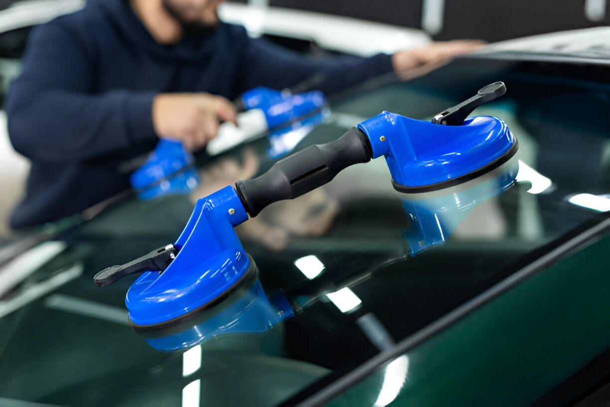 Person using blue suction cups to lift a car windshield.