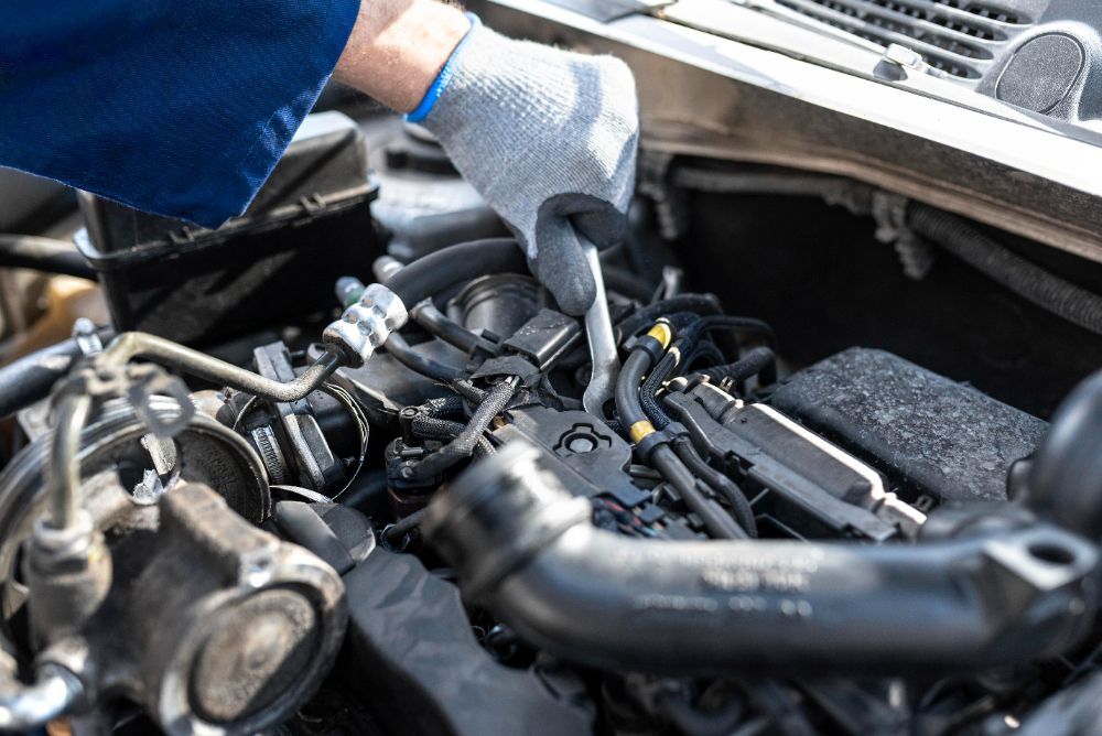 Mechanic working on car engine, wearing gloves, in engine bay.