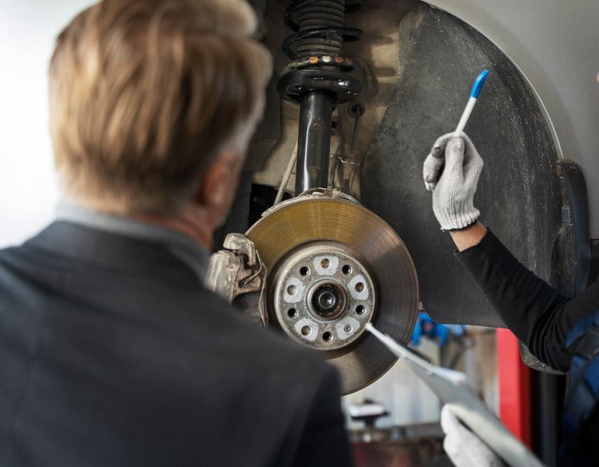 Mechanic pointing to a car's brake disc, explaining to a customer in a garage.