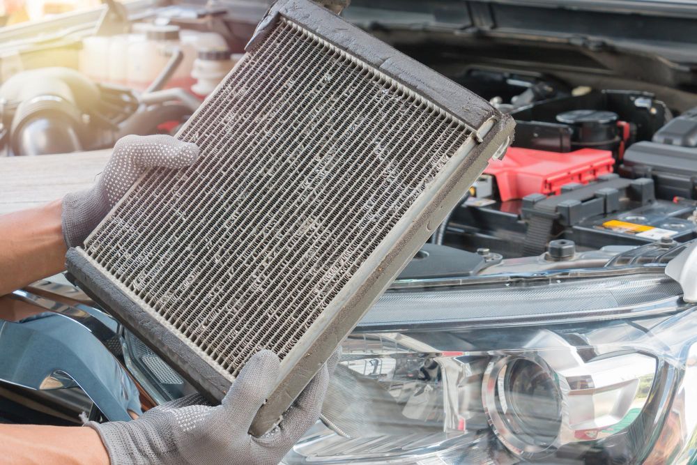 Mechanic holding a dirty car cabin air filter near a car engine.