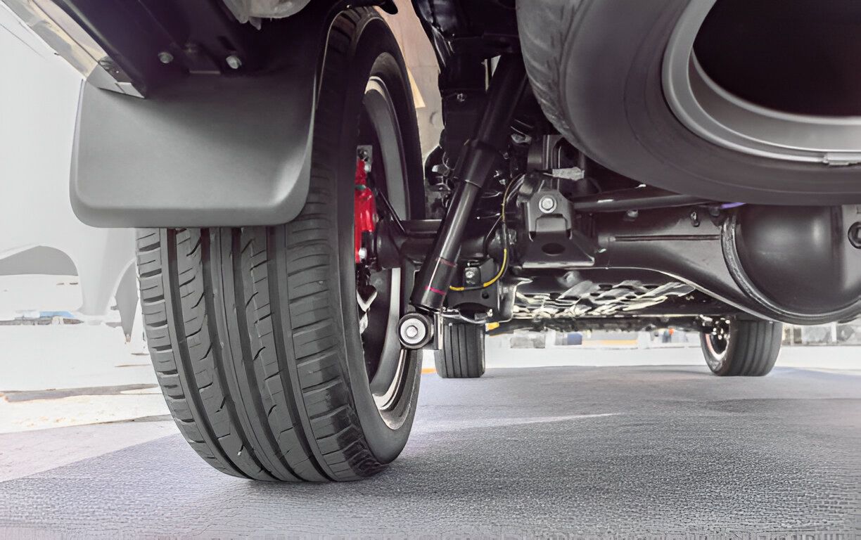 Underside view of a vehicle, showing a tire, suspension, and spare tire. Black and red details.