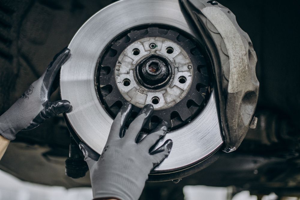 Hands wearing gloves holding a car brake rotor and caliper during a repair.