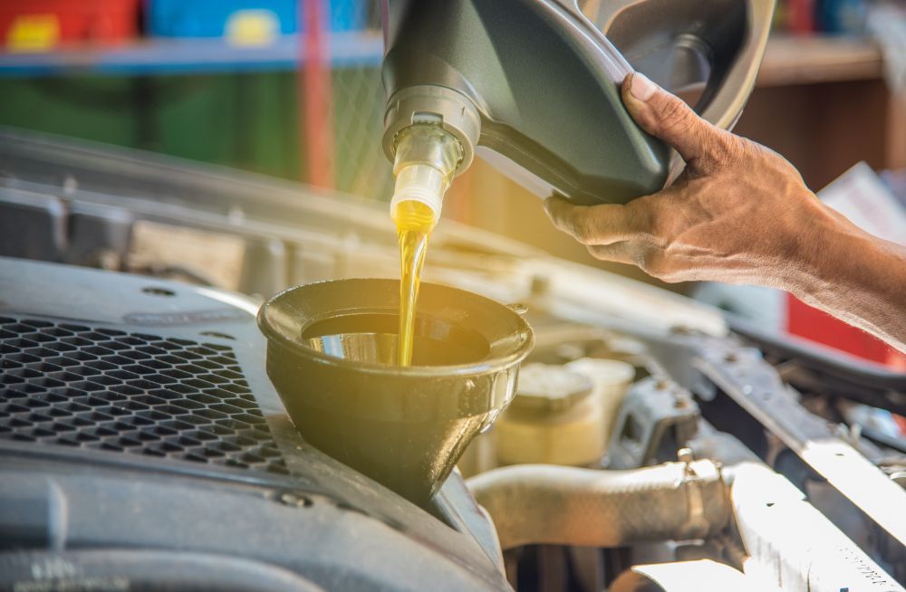 Person pouring oil from a container into a car engine, in a garage.