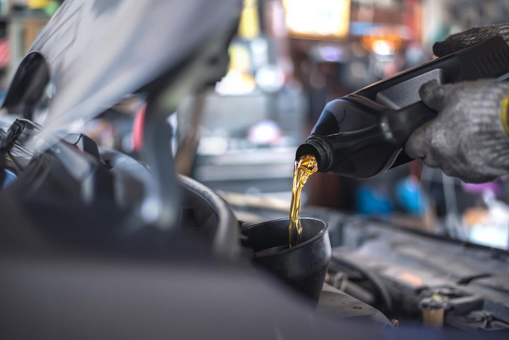 Person pouring oil into a car engine with a funnel in a garage, wearing gloves.