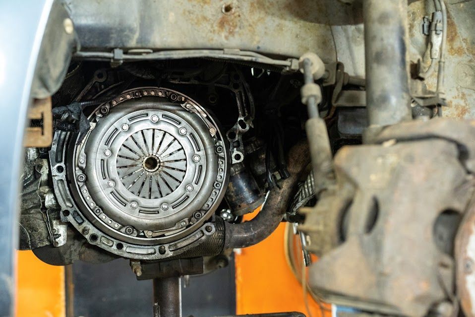 Clutch assembly exposed in an automobile engine bay, showing the clutch disc, pressure plate, and flywheel.
