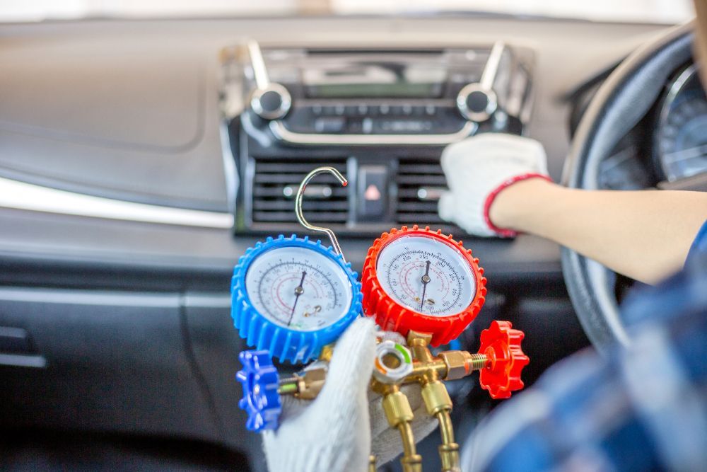 Person in a car checks AC system pressure with gauges.