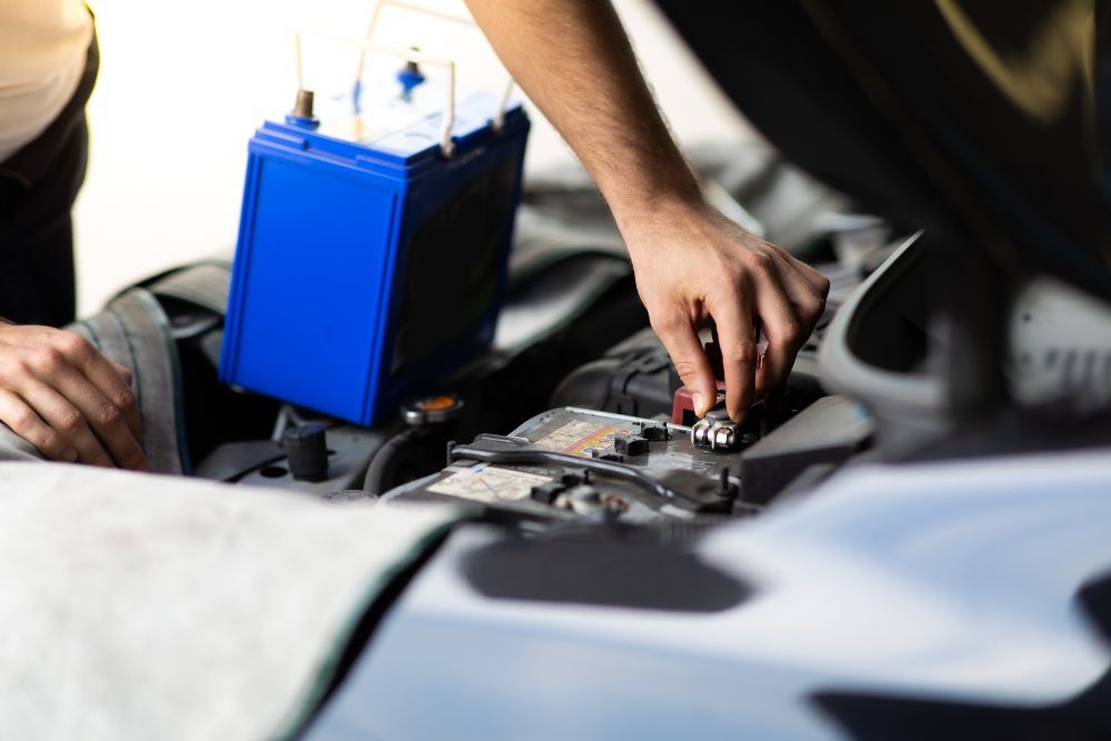 Person connecting a blue car battery in an open engine bay.