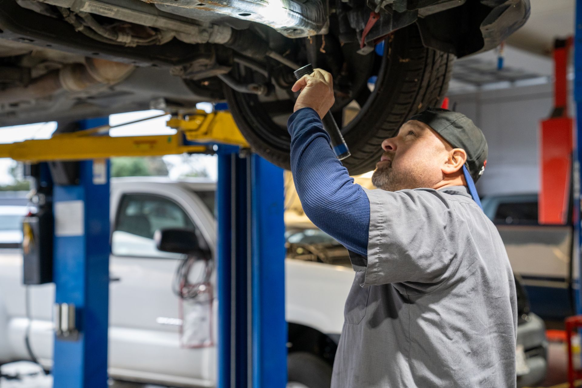 Mechanic under a car on a lift, using a wrench. Garage setting.