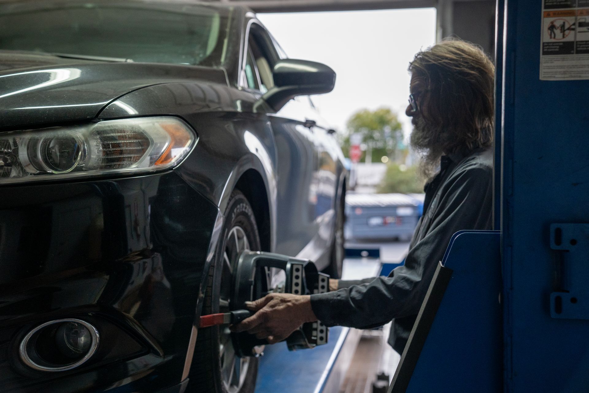 A mechanic with long hair aligns a car wheel at a shop.