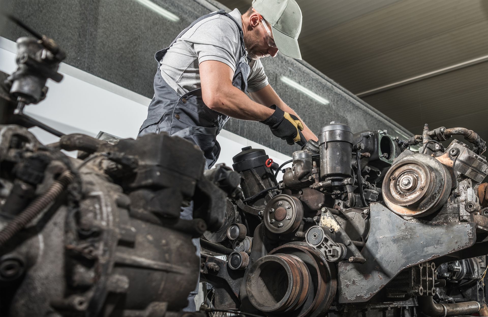 Mechanic working on large engine, wearing overalls and gloves, in a garage setting.