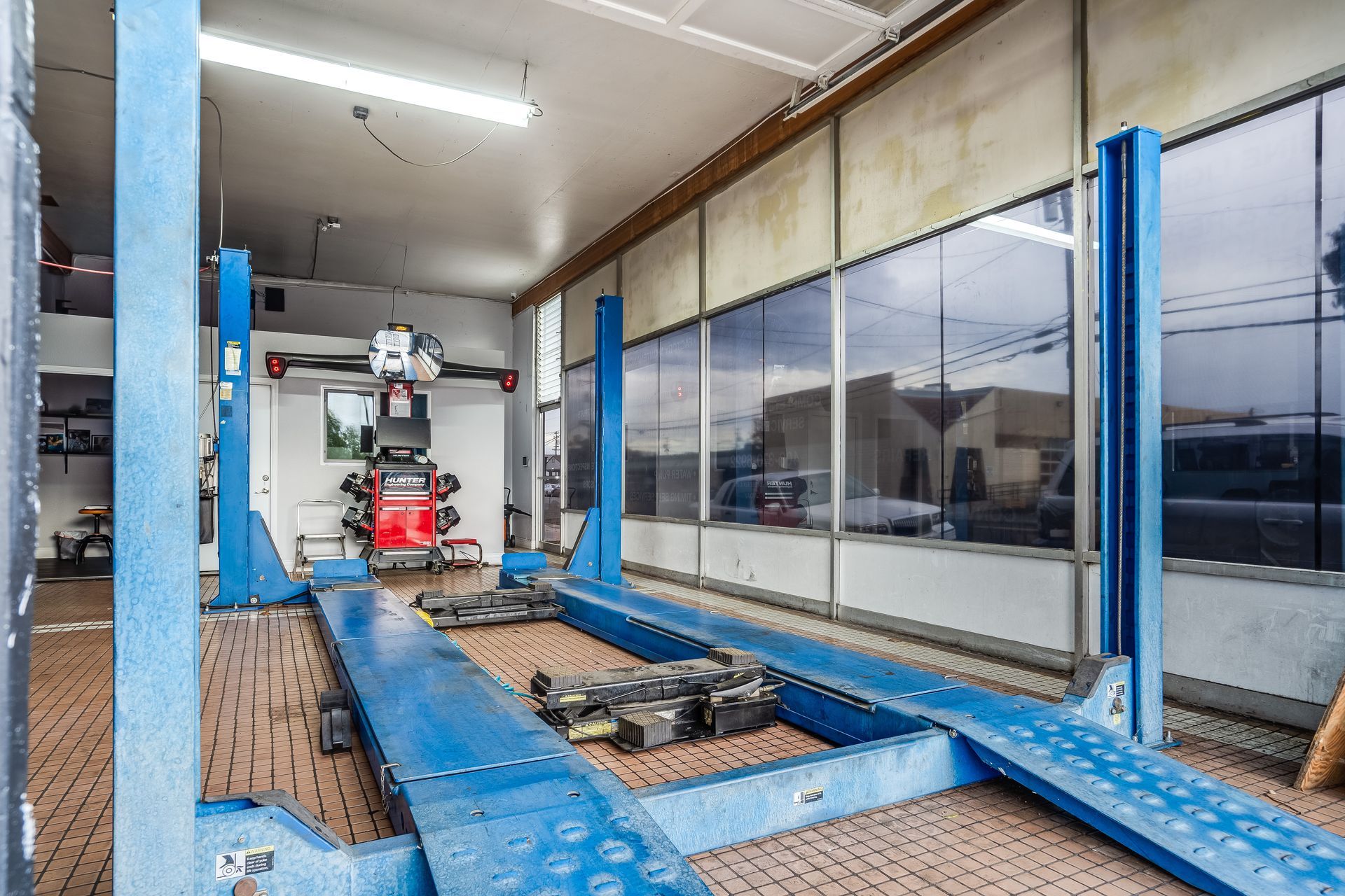 Blue car lift in a car repair shop with alignment equipment and a large window.