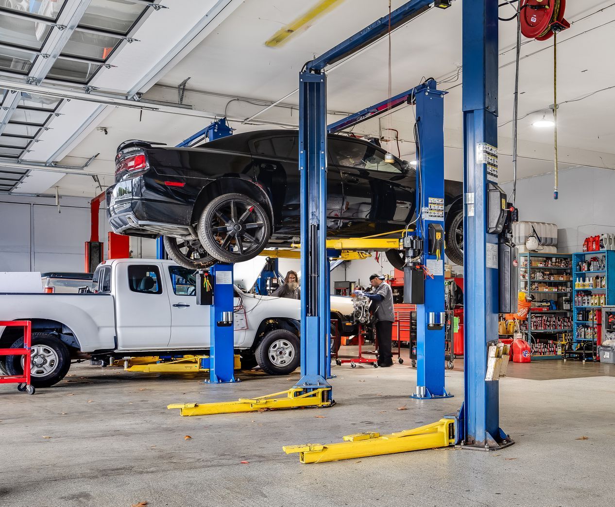 Vehicles on lifts in a garage. Mechanic working on a car, a truck is also lifted, blue and yellow tools.